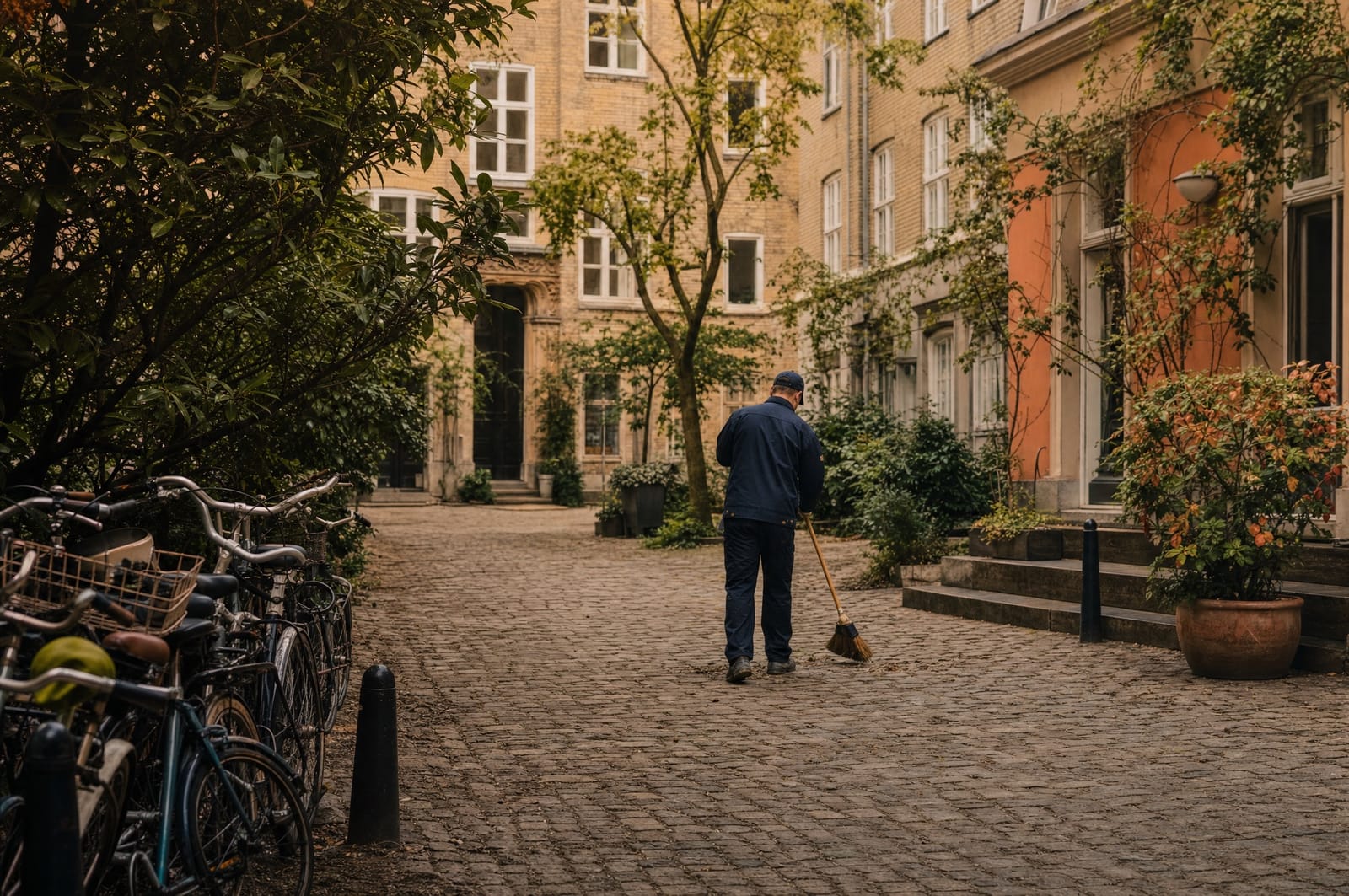 Ejendomsfunktionær fejer brostensbelagt gård ved klassisk københavnsk ejendom