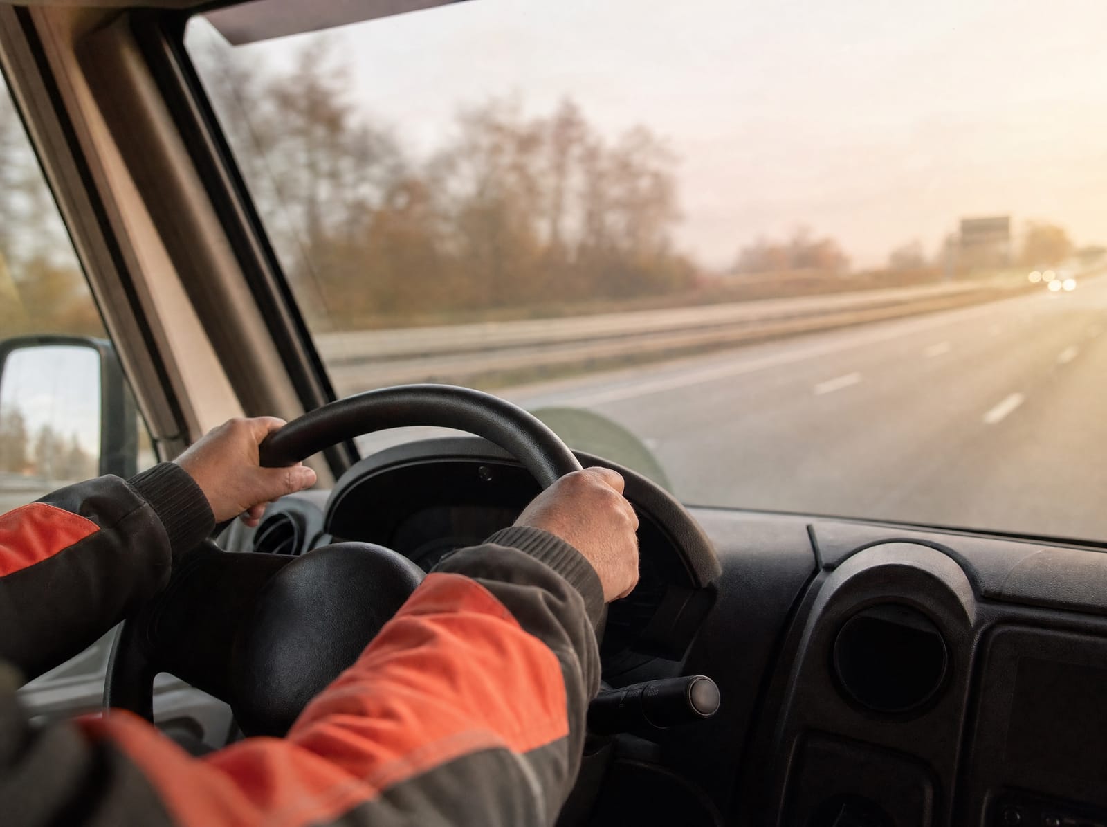 Chaufførens hænder på rattet i en servicevogn på dansk motorvej i morgenlys