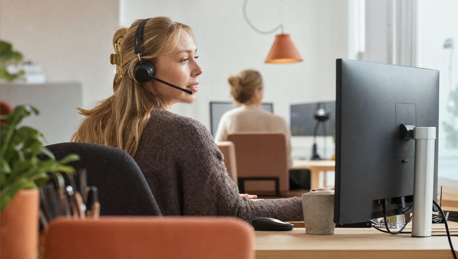 Kundeservicemedarbejder med headset ved skrivebordet i et lyst kontor